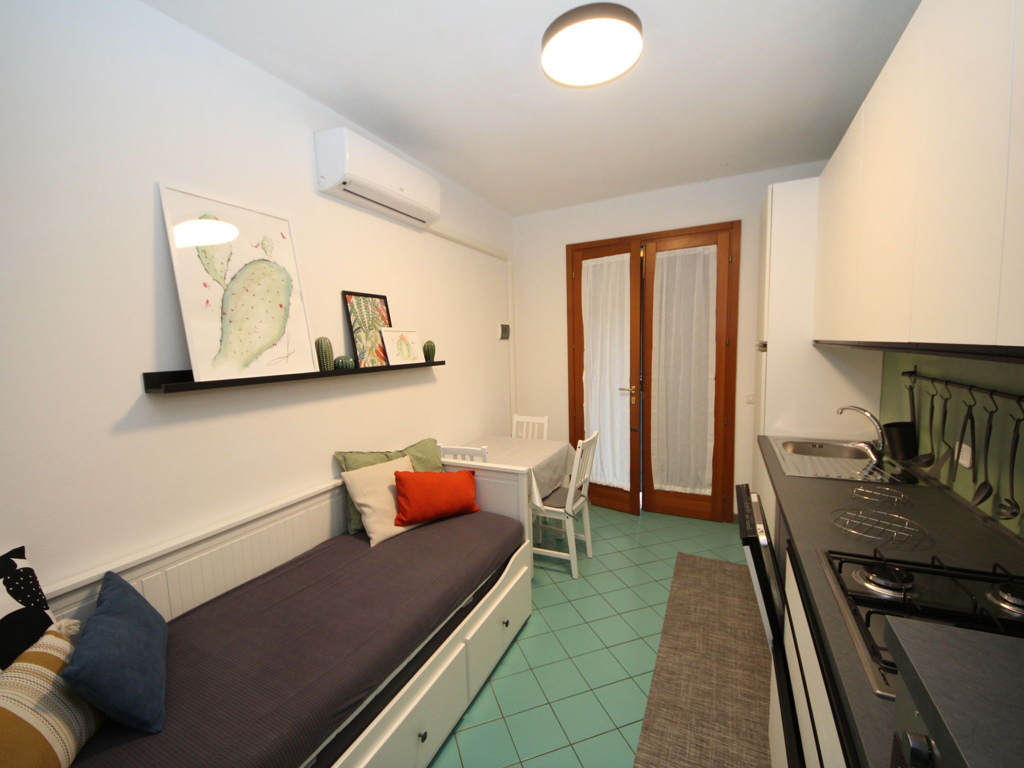 A compact living space with a sofa, a small dining table, a kitchenette with a stove, and a door leading to another room.