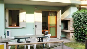 A patio area with a table and chairs, a brick oven, and a small garden. - Solmare by Interhome (Rosolina Mare)