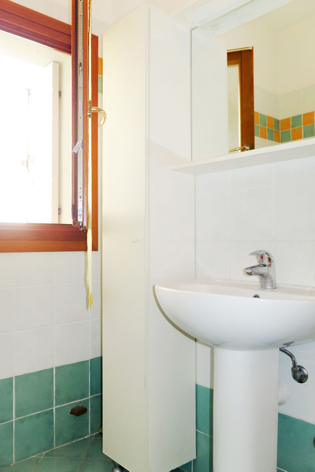Een badkamer met een witte wastafel, een spiegel erboven en een raam met houten kader.