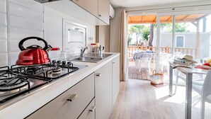 A modern kitchen with a gas stove, a kettle, and a window overlooking a deck.