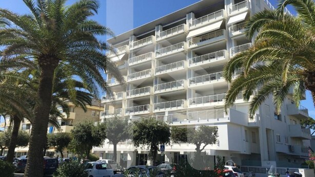 A multi-story hotel with balconies, surrounded by palm trees and parked cars. - Homiday - Riviera D'Orazio (Giulianova)