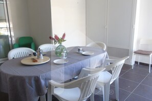 Ein Essbereich mit einem runden Tisch, der mit einer grauen Tischdecke bedeckt ist, weißen Stühlen und einer Vase mit Blumen.