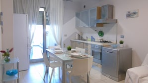 A modern kitchen with white cabinets, a gas stove, and a dishwasher. There is a dining table with chairs and a small plant on the counter. - Homiday - Riviera D'Orazio (Giulianova)