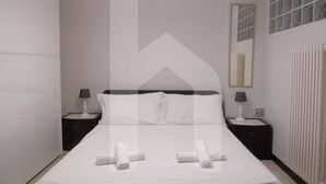 A hotel room with a large bed, two bedside tables with lamps, a mirror, and a radiator. - Homiday - Riviera D'Orazio (Giulianova)