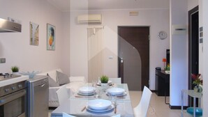 A modern kitchen with a dining area, featuring a stove, oven, and a glass dining table set with plates and cutlery. - Homiday - Riviera D'Orazio (Giulianova)