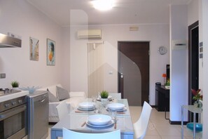 A modern kitchen with a dining area, featuring a stove, oven, and a glass dining table set with plates and cutlery. - Homiday - Riviera D'Orazio (Giulianova)