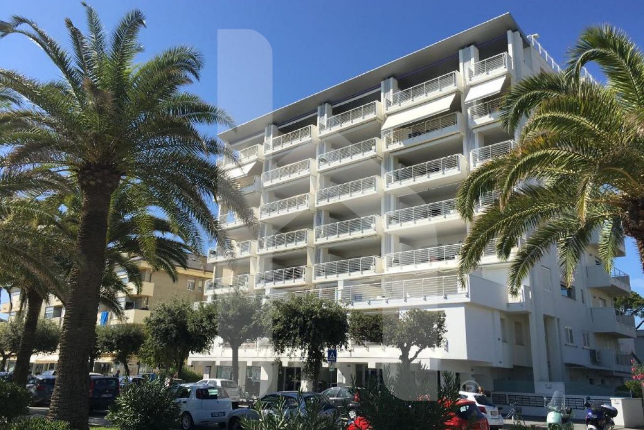 Een meerhoog hotel met balkons, omgeven door palmbomen en geparkeerde auto's.
