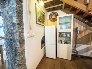 A kitchen with a refrigerator, a hanging light fixture, and a decorative wall hanging.