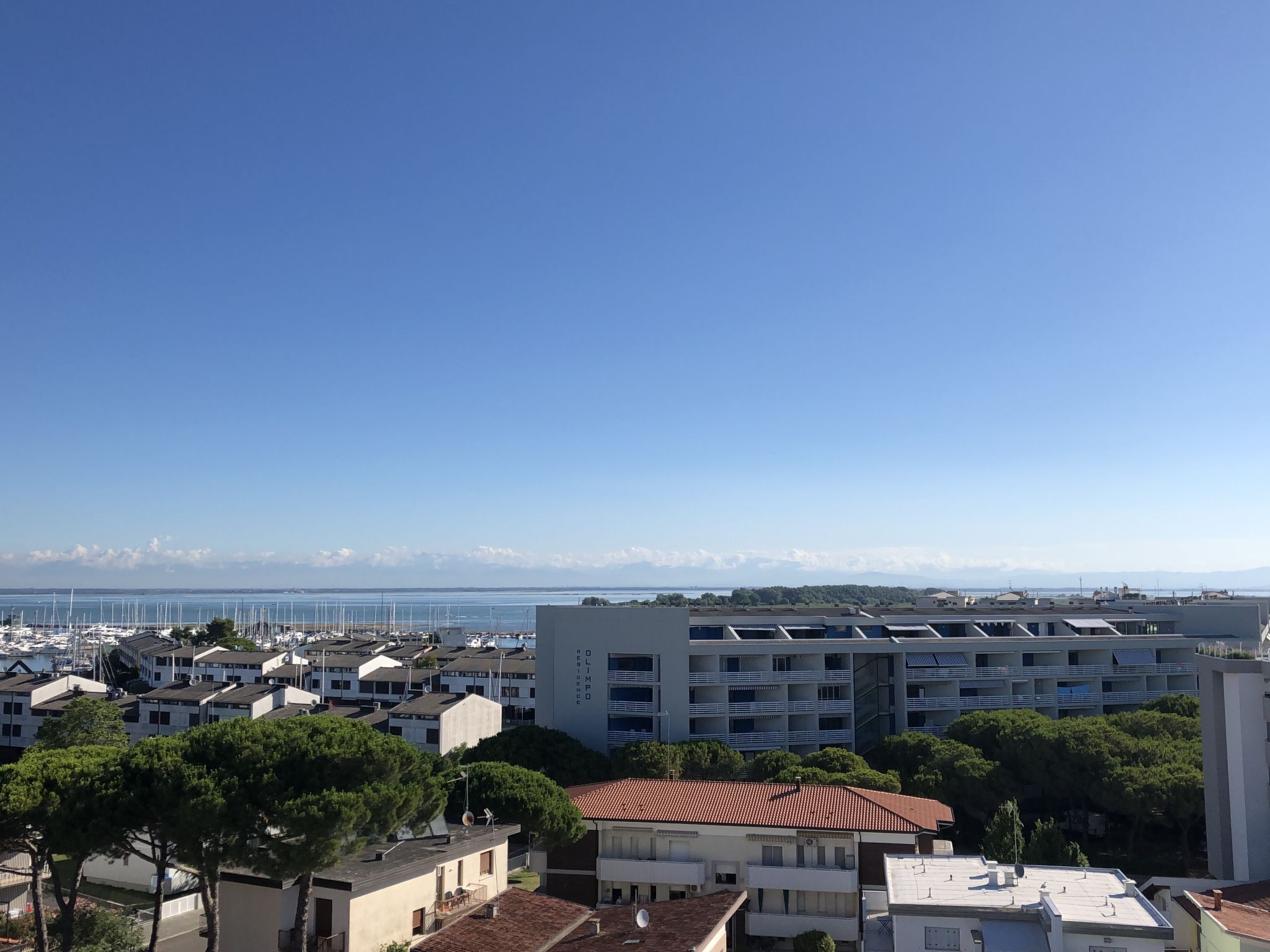 Una zona urbana costiera con edifici residenziali, un porto turistico e un cielo azzurro limpido.