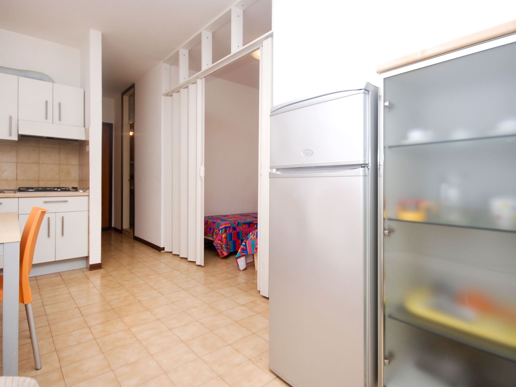 Eine kleine Küche mit weißen Schränken, einem Kühlschrank und einem Essbereich mit einem Stuhl.