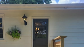 A wooden deck with a door, a hanging planter with greenery, and a potted flower arrangement.