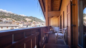 Un balcón de madera con sillas de mimbre, una mesa y vistas a un pueblo de montaña.