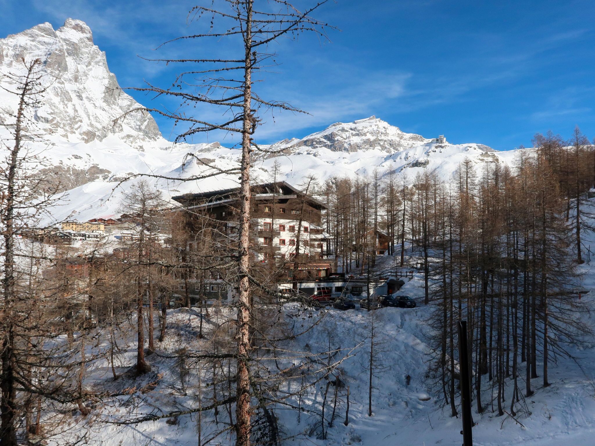 A mountain lodge with a traditional architectural style, surrounded by snow-covered mountains and sparse trees.
