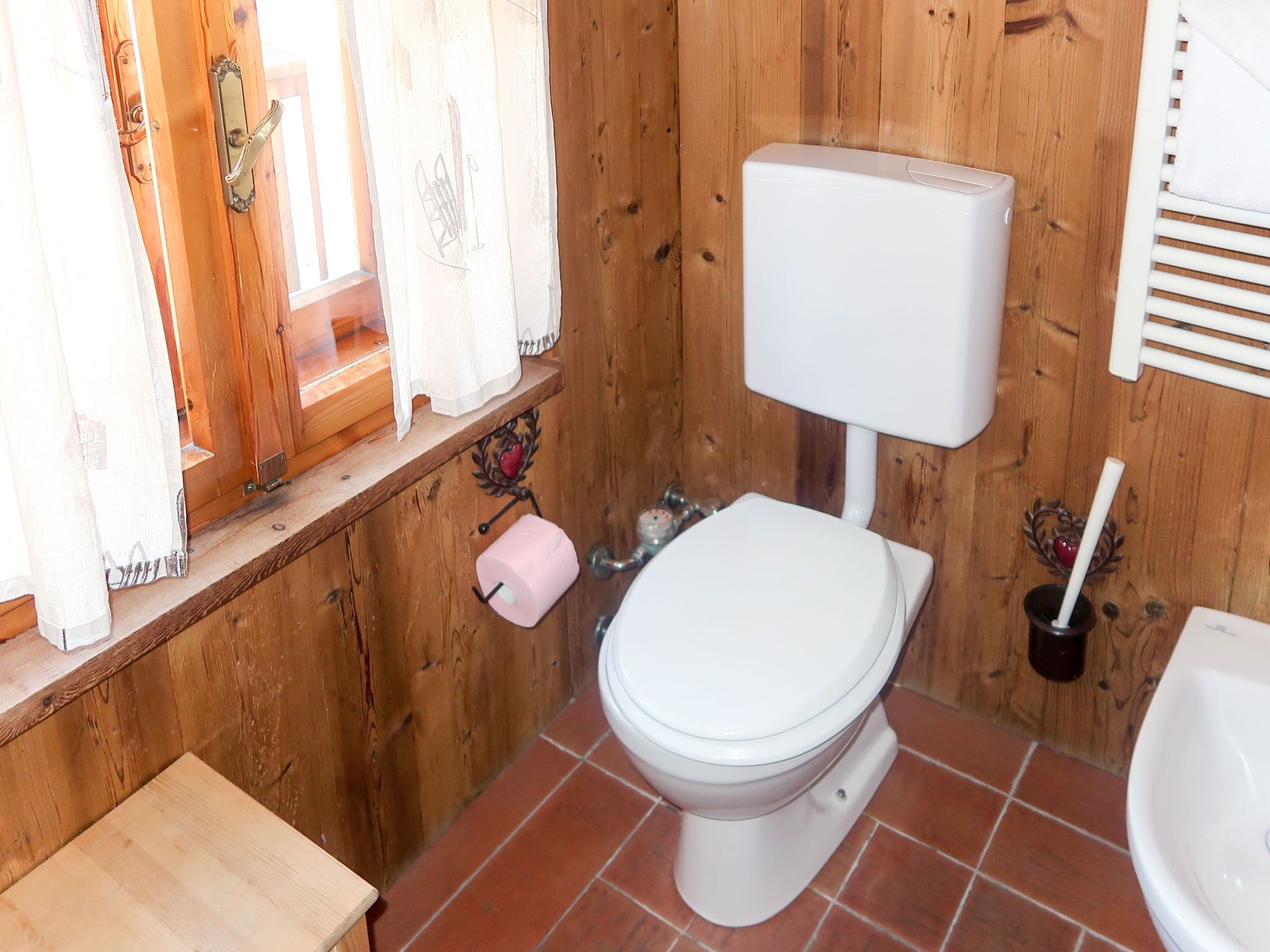 A wooden-paneled bathroom with a white toilet, a pink toilet paper holder, and a white sink.