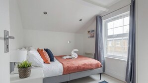 Une chambre moderne avec un lit, une table de chevet avec une lampe et une plante, une fenêtre avec des rideaux et une vue sur l’extérieur.