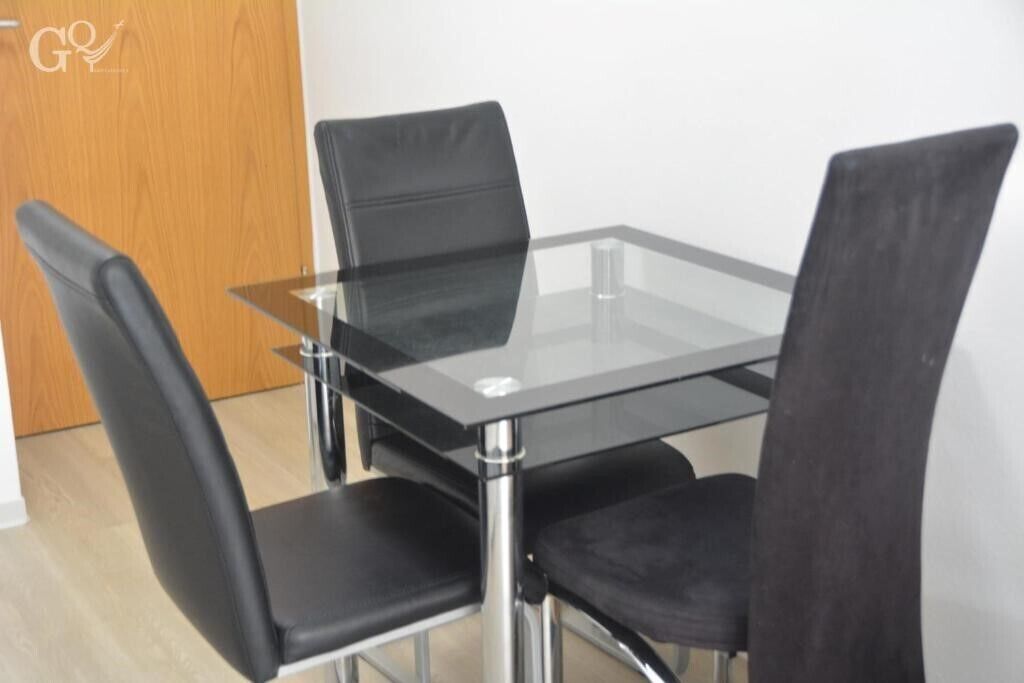 Un comedor moderno con una mesa de vidrio y cuatro sillas negras.