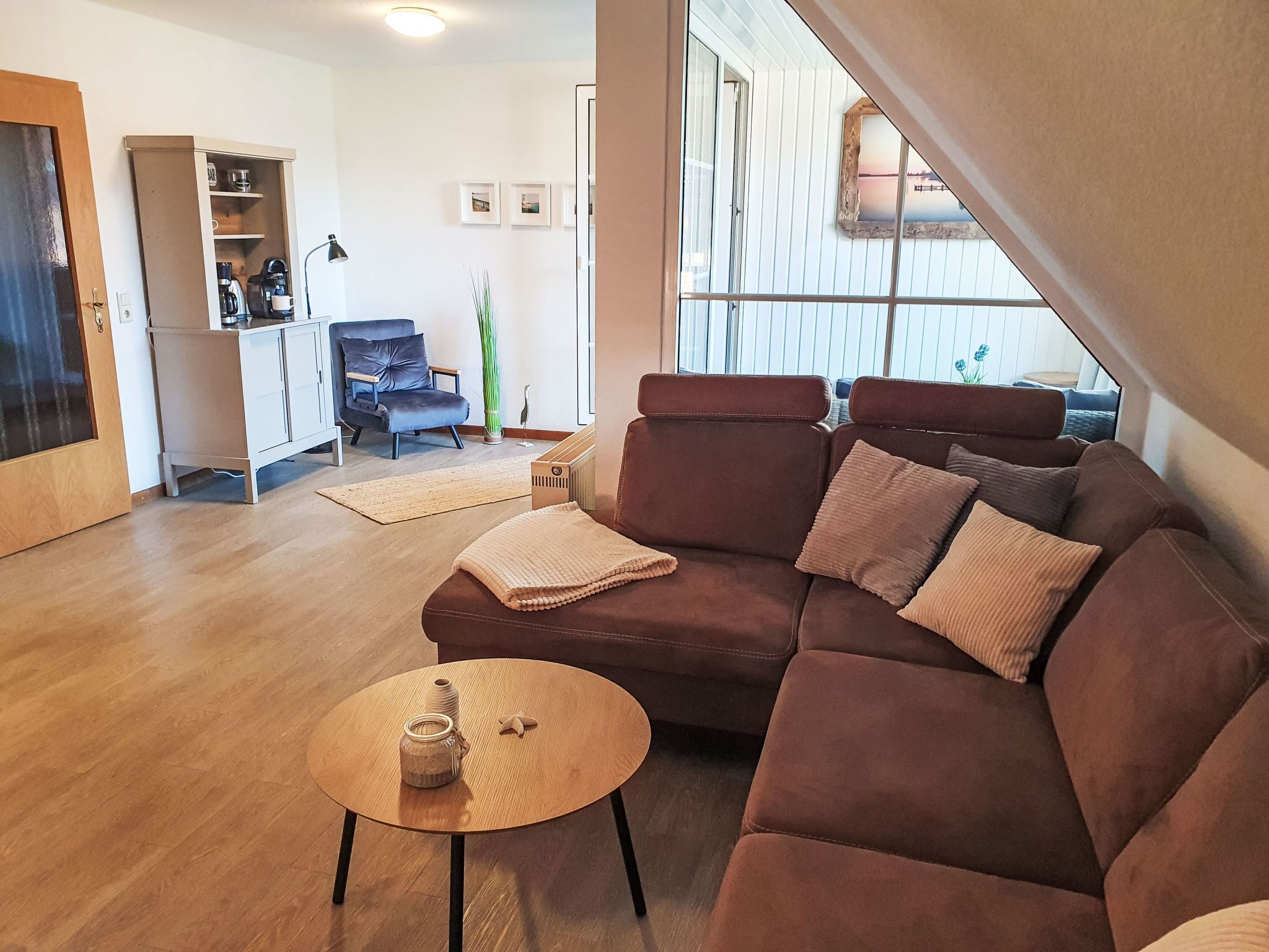 En moderne stue med en brun sofa, et rundt sofabord og et køkken i baggrunden.