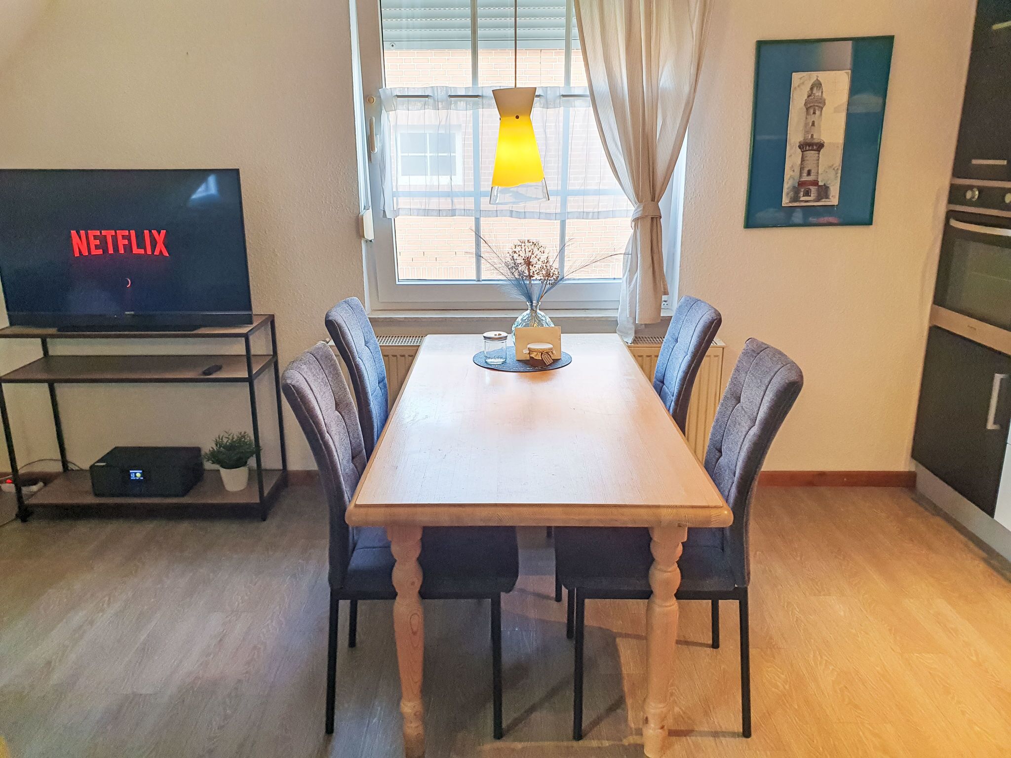 A dining area with a table and chairs, a television displaying 'NETFLIX', and a window with curtains.