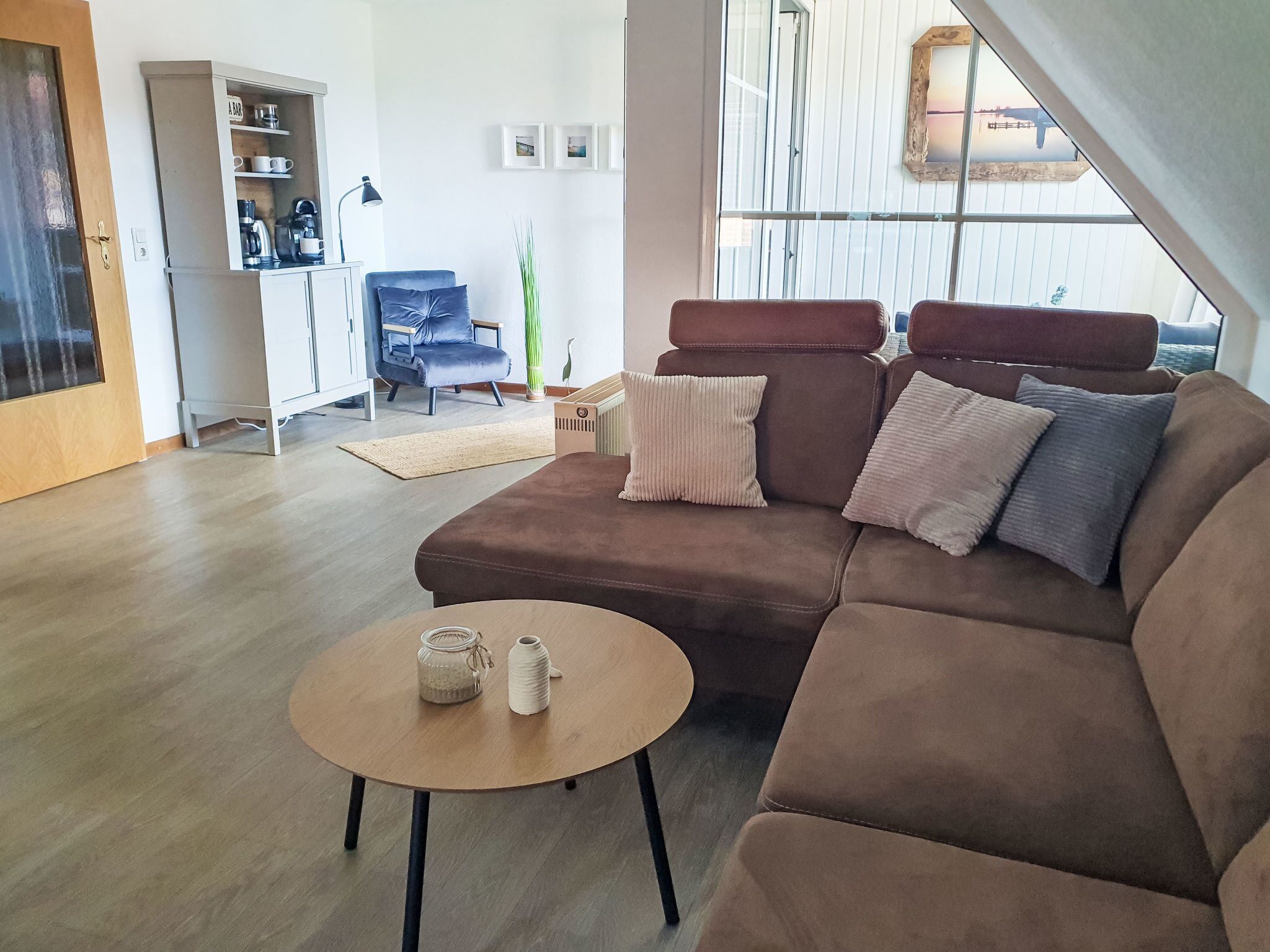 A modern living room with a brown sectional sofa, a round wooden coffee table, and a kitchenette area with a bar.