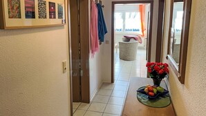Käytävän lattia on laatoitettu, siinä on puuovi ja seinällä on kehystetty taideteos.