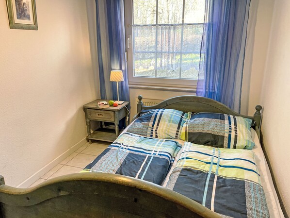 A bedroom with a bed, a nightstand, a lamp, and a window with curtains. - im Dörp by Interhome (Waase)