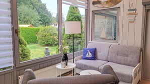 A cozy room with a grey sofa, a small white table, and a lamp. A window offers a view of greenery outside. - Vacation home Karli by Interhome (Loissin)