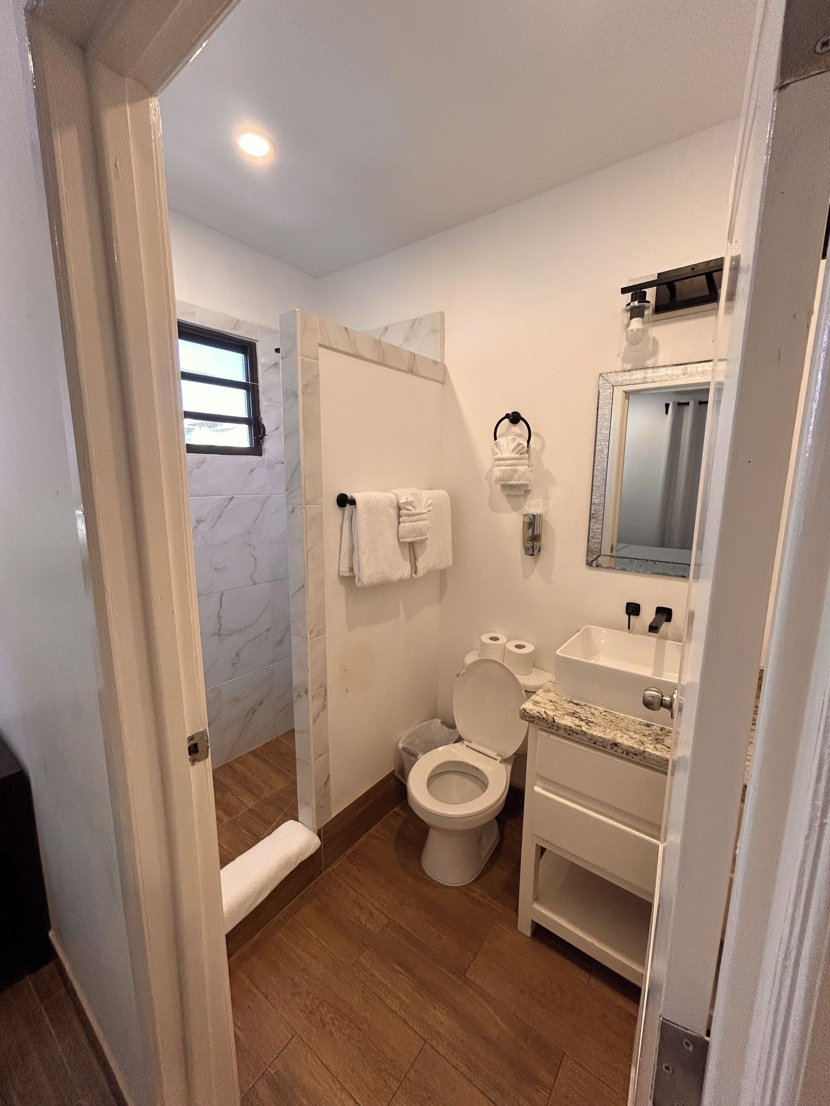 A bathroom with a marble wall, a toilet, a sink, and a shower.