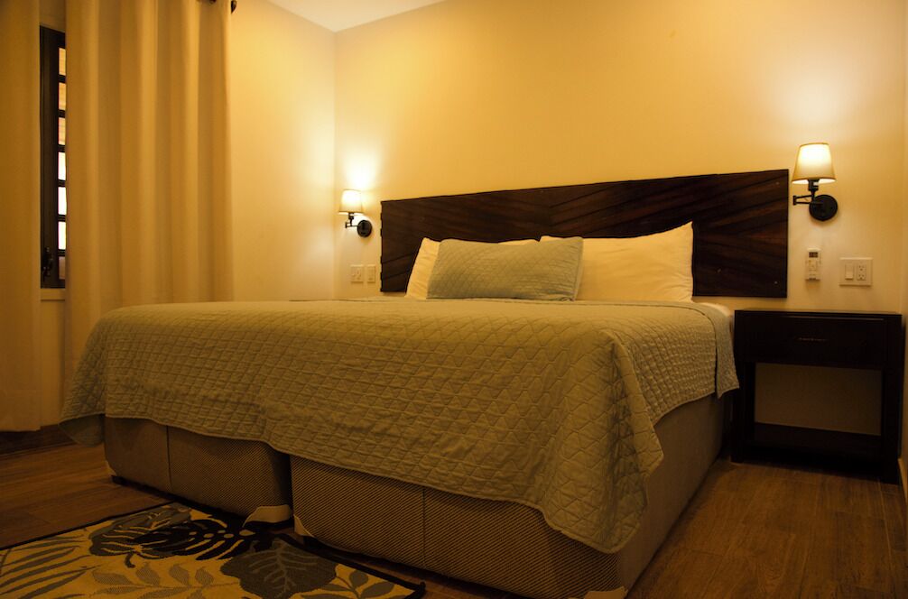 A hotel room with a bed, a nightstand, a lamp, and a window with curtains.