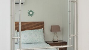 Espejo con marco de bambú que refleja una cama, una mesita de noche y una lámpara de pared.