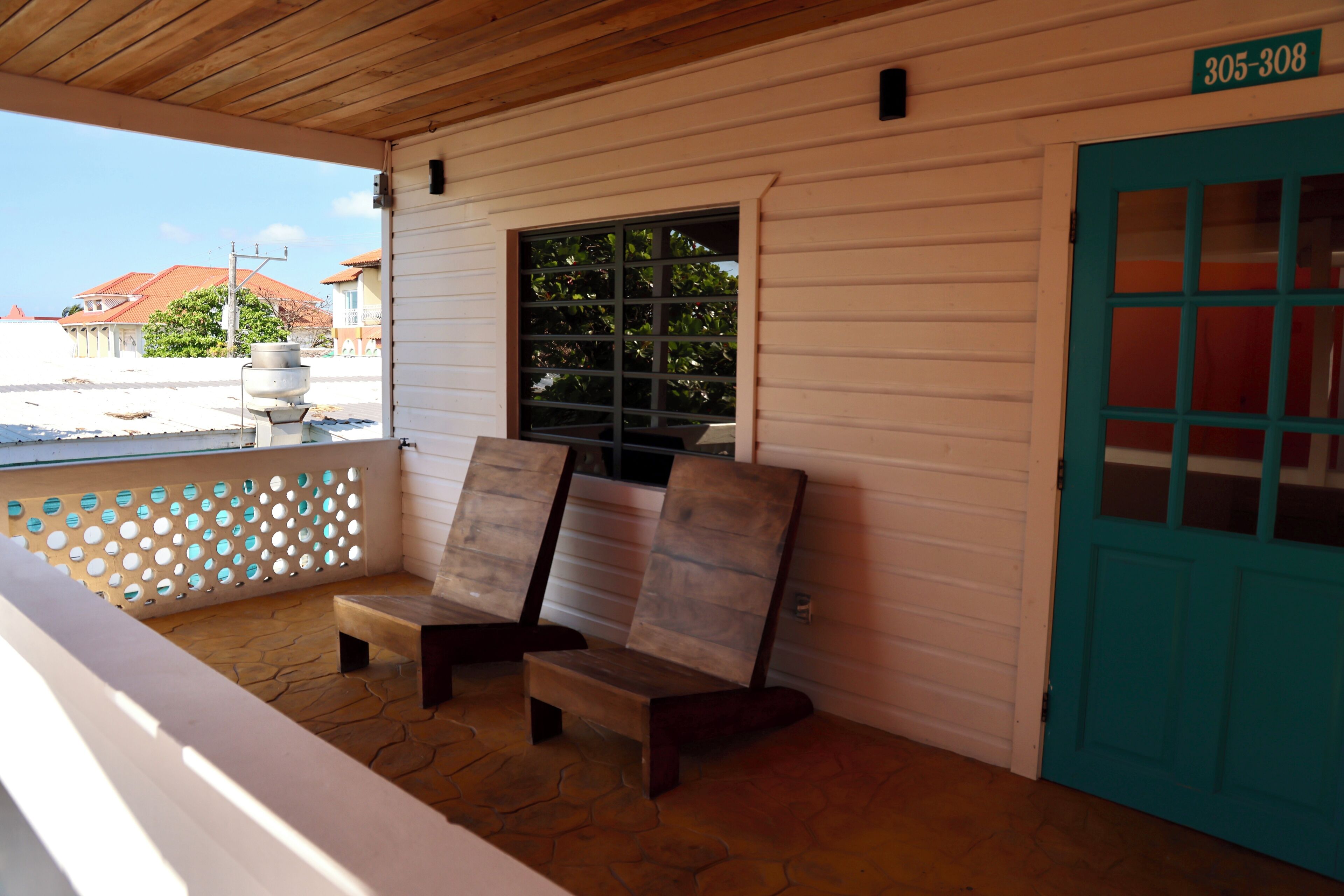 A covered porch with two wooden benches, a window with a grid pattern, and a turquoise door with a number sign above it.