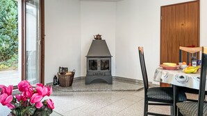 A room with a fireplace, a dining table with chairs, a window with curtains, and a vase of flowers.