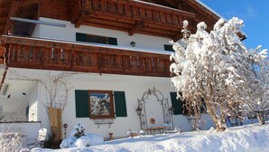 Een houten chalet met twee verdiepingen, een balkon, een eethoek en een tuin bedekt met sneeuw.