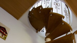 Een wenteltrap met houten treden en witte balustrades, die uitkomt op een plateau met uitzicht op een witte muur en een raam.