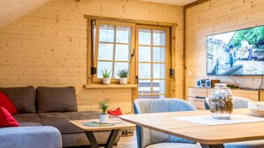 Una habitación acogedora con decoración de madera, un sofá, una mesa de comedor y un televisor mostrando una escena.