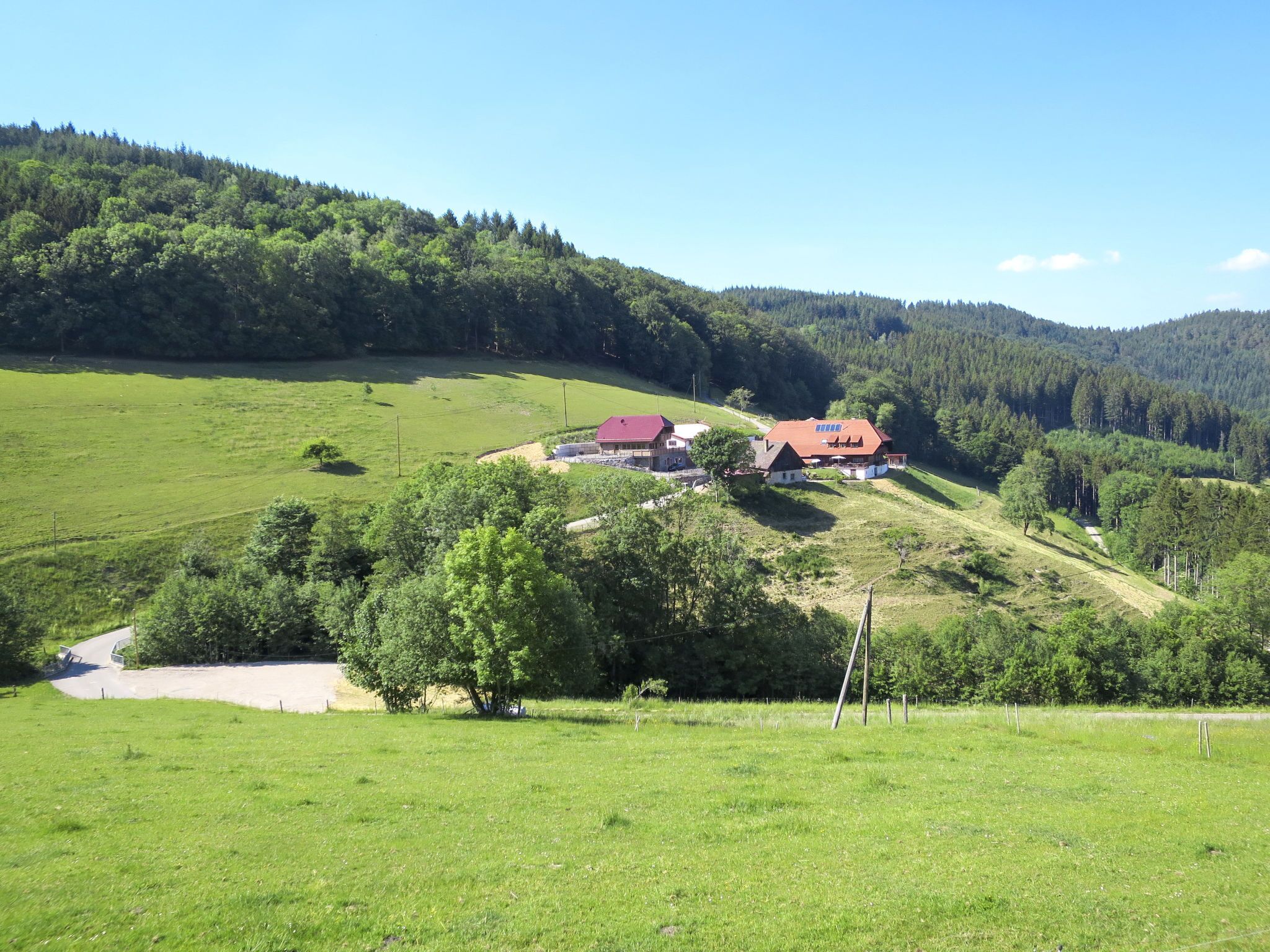 A rural landscape with a large house surrounded by green fields and forested hills.