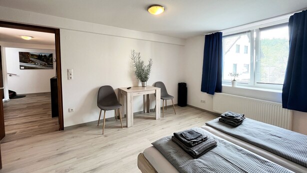 Ett modernt hotellrum med en säng, ett litet bord med stolar, en krukväxt och utsikt över omgivningen.