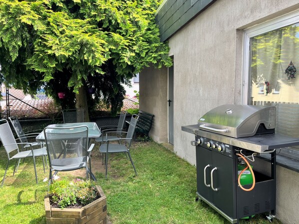 Eine Terrasse im Freien mit Grill, Metallstühlen und einem Tisch.