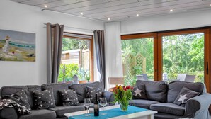 A modern living room with a grey sofa set, a white coffee table, and a view of greenery outside. - Deichhaus Küstenwind by Interhome (Fedderwardersiel)