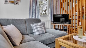 Ett mysigt vardagsrum med en grå soffa, ett TV-bord i trä och ett soffbord i glas.