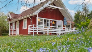 Ett rött trähus med en vit veranda och en trädgård med blå blommor.