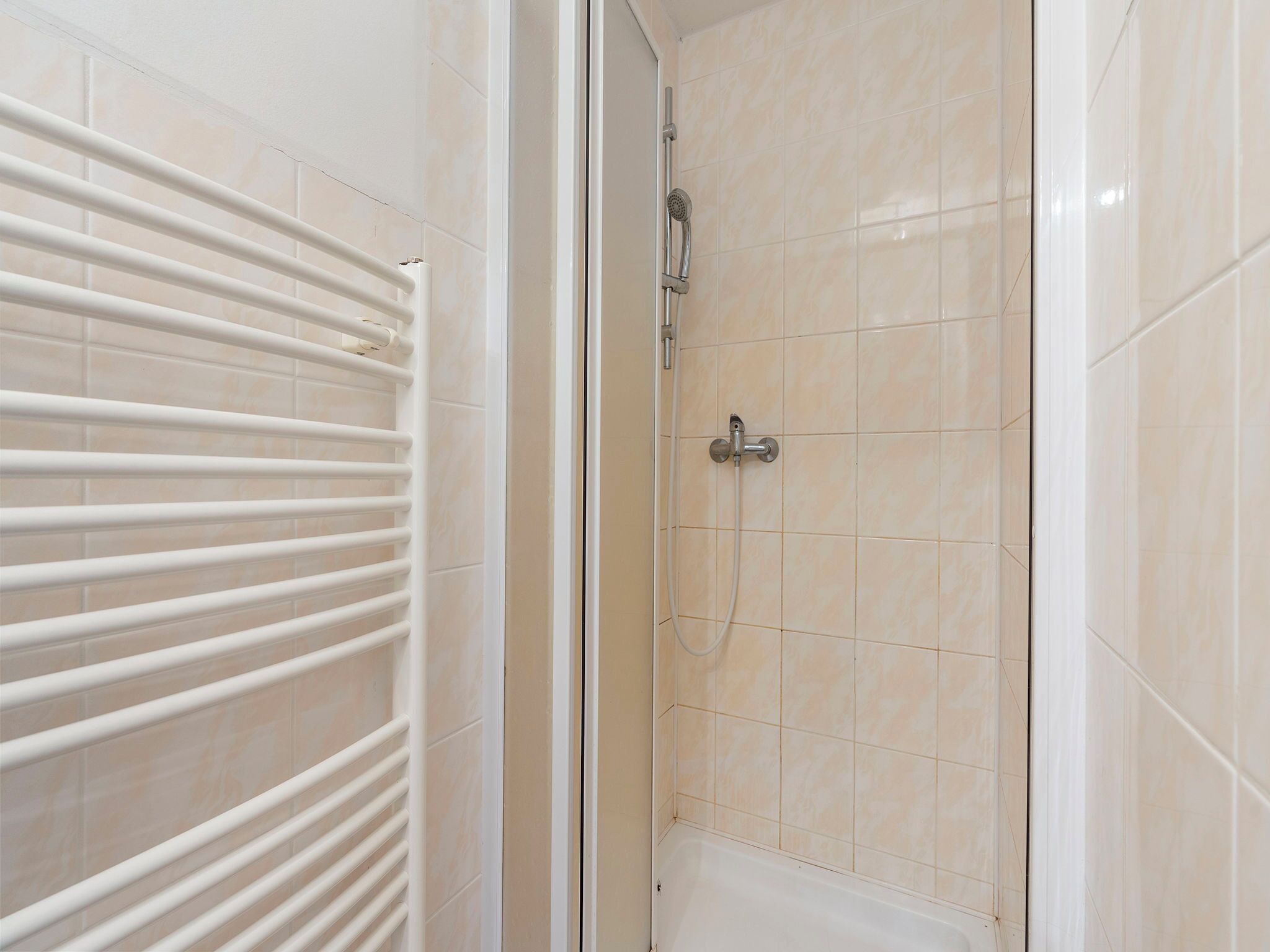 Une salle de bain avec des murs carrelés de couleur beige, une baignoire blanche et un porte-serviettes blanc.