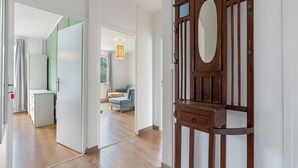 A hallway with a wooden door, a white wall, and a glimpse of a living area with a sofa and a table. - Lužnice by Interhome (Tyn nad Vltavou)