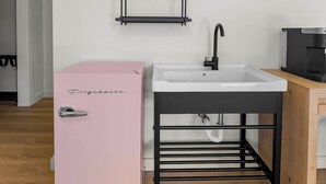 Een kleine keuken met een roze koelkast, een wit spoelgedeelte en een zwart metalen plankensysteem.