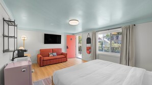 Een slaapkamer met een bed, een rode bank, een televisie en een raam met gordijnen.