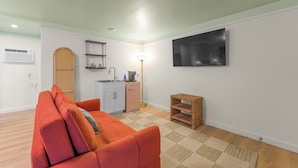 Een compacte leefruimte met een kitchenette, een bank, een televisie en een klein houten bijzettafeltje.