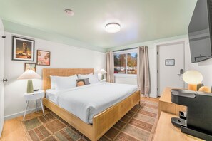 Quarto de hotel com cama, abajures, televisão, escrivaninha com luminária e janela com cortinas.