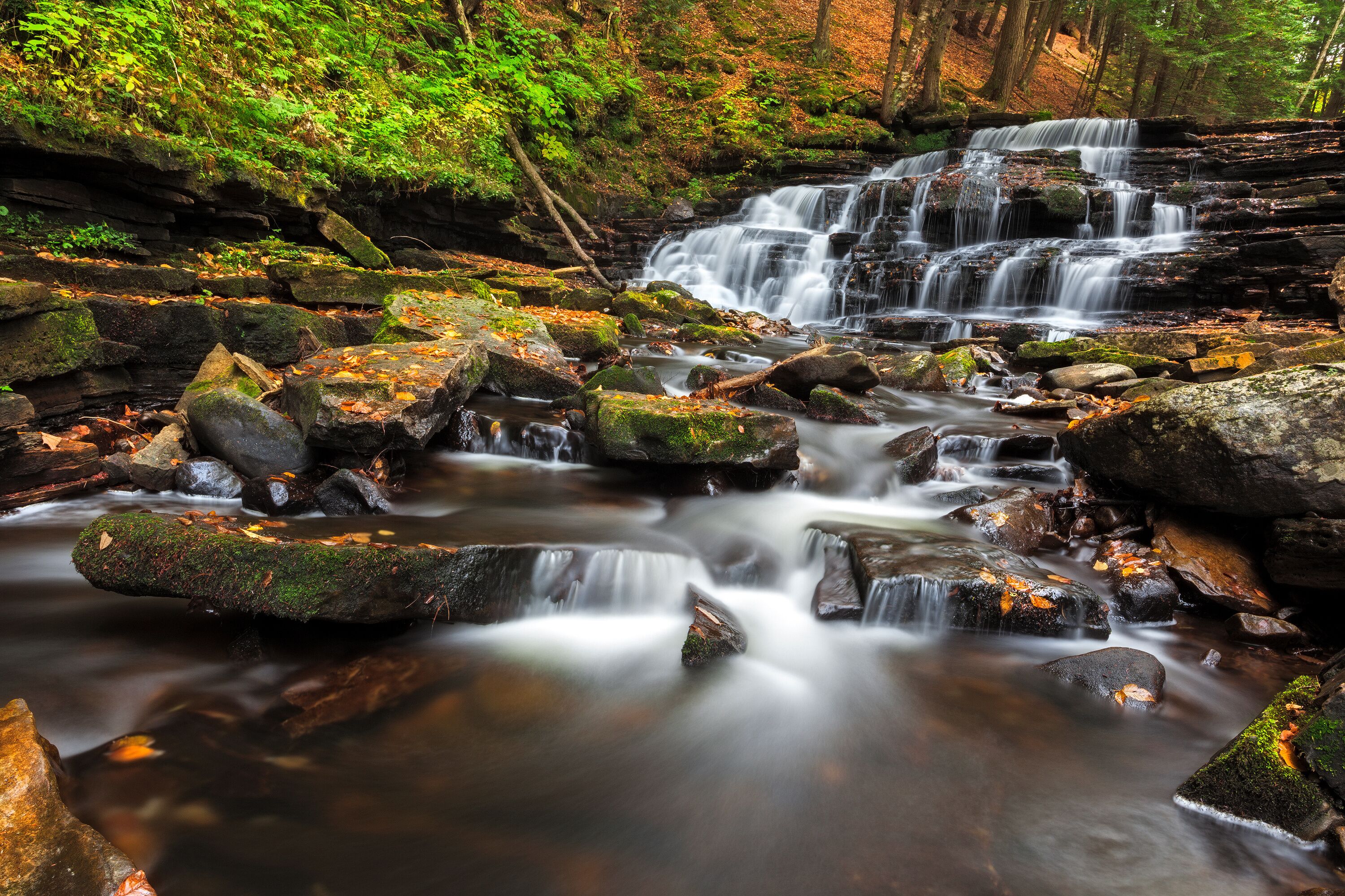 A multi-tiered waterfall in a forested area with rocks and moss.