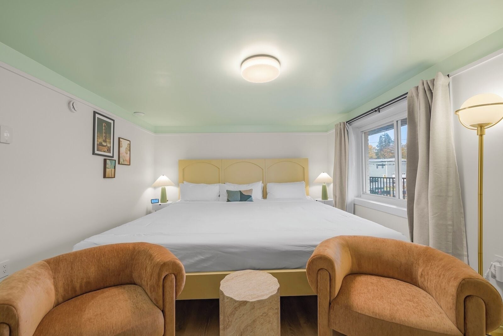 A hotel room with a large bed, two armchairs, a small round table, and a window with curtains.