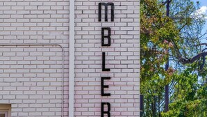 Een gebouw met een witte bakstenen gevel en een bord waarop 'THE AMBLER' staat.