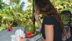 Eine Person sitzt an einem Tisch mit einer grünen Vase, rosa Blumen und einem weißen Fächer.